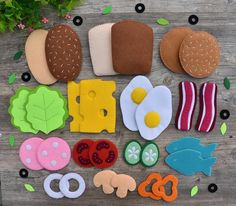 several felt food items laid out on a wooden table next to flowers and leaves,