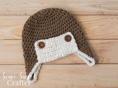 a crocheted brown and white hat with buttons on the side sitting on a wooden surface