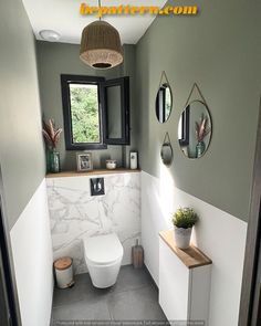 a white toilet sitting next to a window in a bathroom under a light fixture with three mirrors on the wall