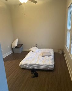 an empty bedroom with a bed and ceiling fan in it's corner, next to a window