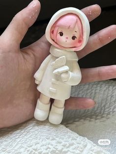 a hand holding a small toy doll in it's right hand and wearing a white coat