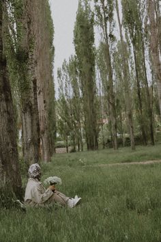 a person sitting in the grass with an umbrella next to some trees and looking at their cell phone