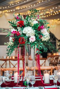 a tall vase filled with flowers and greenery on top of a red table cloth