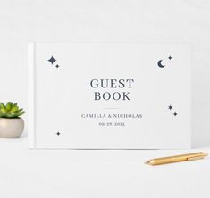 a guest book next to a pen and succulent on a white surface with stars