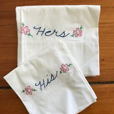 two white towels with embroidered words on them sitting on a wooden floor next to each other