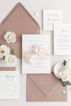 the wedding stationery is laid out on top of an envelope, with white flowers and greenery