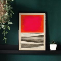 a red and black painting sitting on top of a shelf next to a potted plant