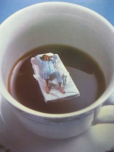 a cup of coffee with a woman laying on top of it and wrapped in a piece of paper