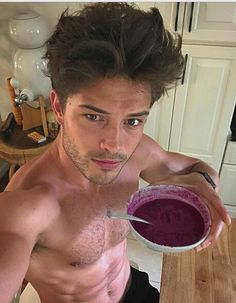 a shirtless man is holding a bowl of purple liquid and looking at the camera