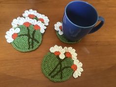 two crocheted coasters with flowers on them next to a coffee cup and mug