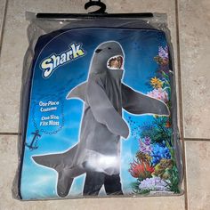 an adult size shark costume is shown in the package on the tile floor with its mouth open