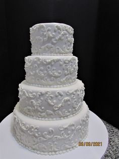 a three tiered white wedding cake sitting on top of a table next to a black wall