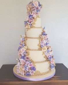 a three tiered wedding cake with purple flowers on the side and gold trimmings