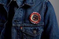 a person wearing a denim jacket with a tie - dyed pin on it