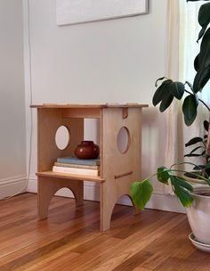 a small wooden shelf sitting on top of a hard wood floor next to a potted plant