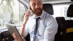 a man sitting in the back seat of a car talking on his cell phone and holding a tablet