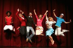 a group of people jumping in the air with their hands up on a red stage