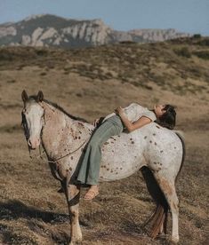 a woman riding on the back of a brown and white horse in an open field