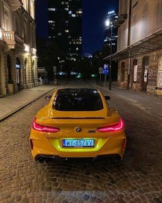 the rear end of a yellow sports car parked on a cobblestone street at night