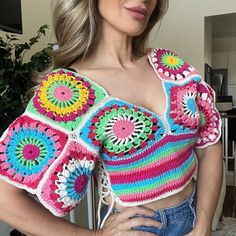 a woman wearing a colorful crochet top posing for the camera with her hands on her hips