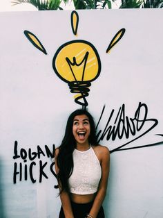 a woman standing in front of a wall with a lightbulb on it's head