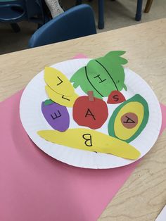 a paper plate with fruit and vegetables cut out on it sitting on a pink table