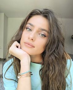 a woman with long brown hair wearing a blue shirt and bracelets, looking at the camera