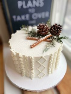 a white frosted cake with pine cones and cinnamon sticks sitting on top of it