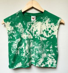 a green and white tie - dyed shirt hanging on a wooden hanger against a wall