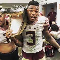 a football player holding a large alligator in his hand and another man standing behind him