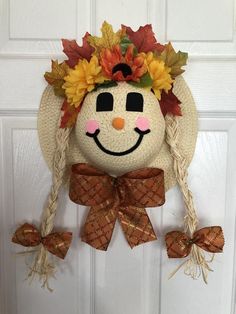 a scarecrow head hanging on a door with fall leaves and sunflowers around it