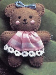 a brown teddy bear wearing a pink and white dress sitting on top of a green leaf