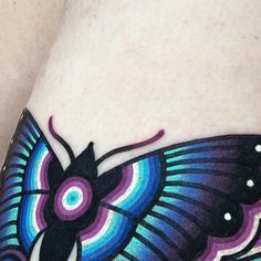 a colorful butterfly tattoo on the side of a woman's leg, with white dots around it