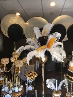 a table topped with lots of cakes and desserts covered in black, white and gold decorations