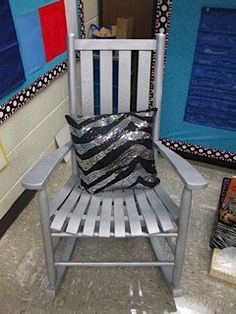 a white chair with a black and silver pillow on it in front of a wall