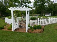 a white fenced in garden area with trees and shrubs