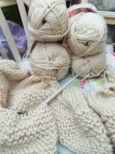 three balls of yarn sitting on top of a white chair next to some knitting needles