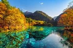 a river surrounded by mountains and trees in the fall season with blue water running through it