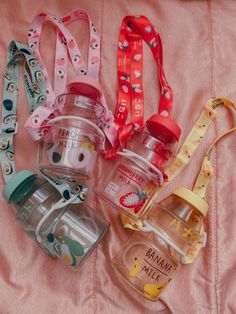 four baby bottles sitting on top of a pink bed next to pacifiers and lanyard