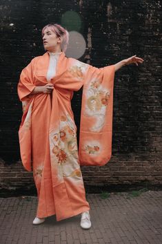 This furisode kimono has a very fun, youthful feel to it. The main colour is a soft orange/pink, best described as salmon. Some spots are left white though, which works as a great calm contrast to the bright colour. The fabric has a cloud and smoke pattern woven into it. This kimono might not be our most extravagantly decorated kimono - but the decorations it has have all been embroidered! The beautiful glistening golden and silver, orange, red, and white threads have been woven into displays of Pink Vintage Long Kimono, Pink Kimono With Kimono Sleeves For Tea Ceremony, Pink Kimono For Tea Ceremony, Pink Kimono For Spring Wedding, Spring Wedding Pink Kimono, Traditional Long Orange Kimono, Traditional Pink Kimono For Spring, Traditional Pink Kimono For Wedding, Pink Robe With Kimono Sleeves For Wedding