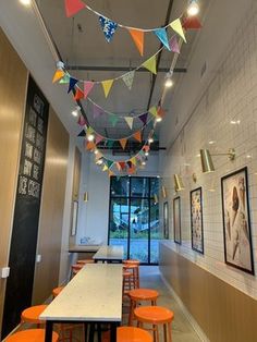 an indoor dining area with tables and orange stools, decorated with bunting flags