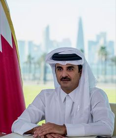 a man sitting at a desk in front of a flag and a cityscape