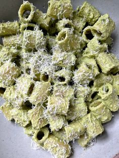 a white bowl filled with green pasta covered in parmesan cheese