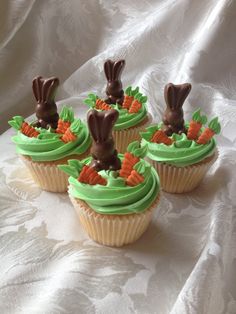 four cupcakes with green frosting and chocolate bunny ears on top, sitting on a white tablecloth