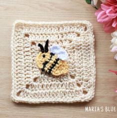 a crocheted square with a bee on it and pink flowers in the background