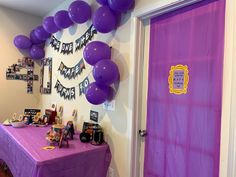 a purple table topped with balloons next to a door and sign that says happy birthday