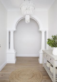 a hallway with white walls and wooden flooring has a chandelier hanging from the ceiling