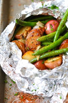 some food that is in tin foil on a table with green beans, potatoes and carrots