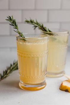 two glasses filled with lemonade and rosemary garnish on a white counter top