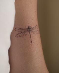 a small dragonfly tattoo on the back of a woman's left arm